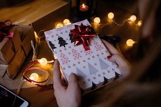 person-holding-gift-box-with-red-ribbon-beside-string-lights-1687049.jpg